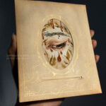 Drawing of an eye in an antique photo frame. The eye is pointed down and to the right, with foliage and blood. Gold drips are on the antique photo frame.