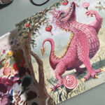 Picture of painting of the candy cane dragon on artist's desk with pain palette next to it