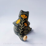 A ceramic tiger sculpture done with a cream white clay and black underglaze with sgraffito markings all over it's body. This shows the back of the piece which features my signature orange California Poppy motif crawling up the tiger's back.