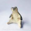 A ceramic tiger sculpture done with a cream white clay and black underglaze with sgraffito markings all over it's body. This shows the front of the piece. The tiger is in a seated-up position almost similar to a human sitting down with their legs splayed out in front of them.