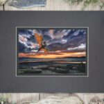 A dragon flies over a beach with driftwood logs, a sunset and ocean in the background.