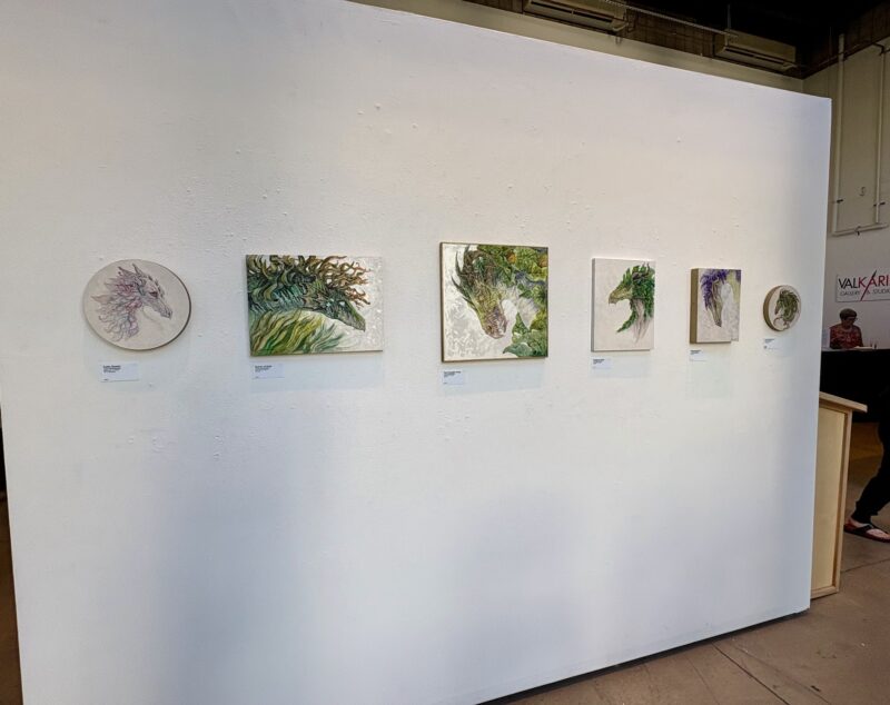 Gallery wall with six floral court dragons on it, from left to right "Calla Queen", "The. Queen of Kelp", "The Pumpkin King", "Knight of Holly", "Prince of Wisteria", and "Lavender Emperor"