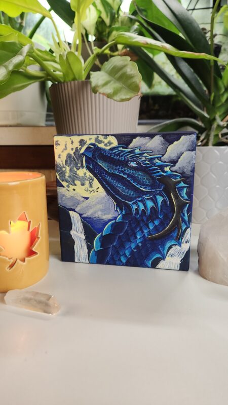 A painting of a blue dragon on a canvas sitting in a table surrounded by candles and crystals with plants in the background