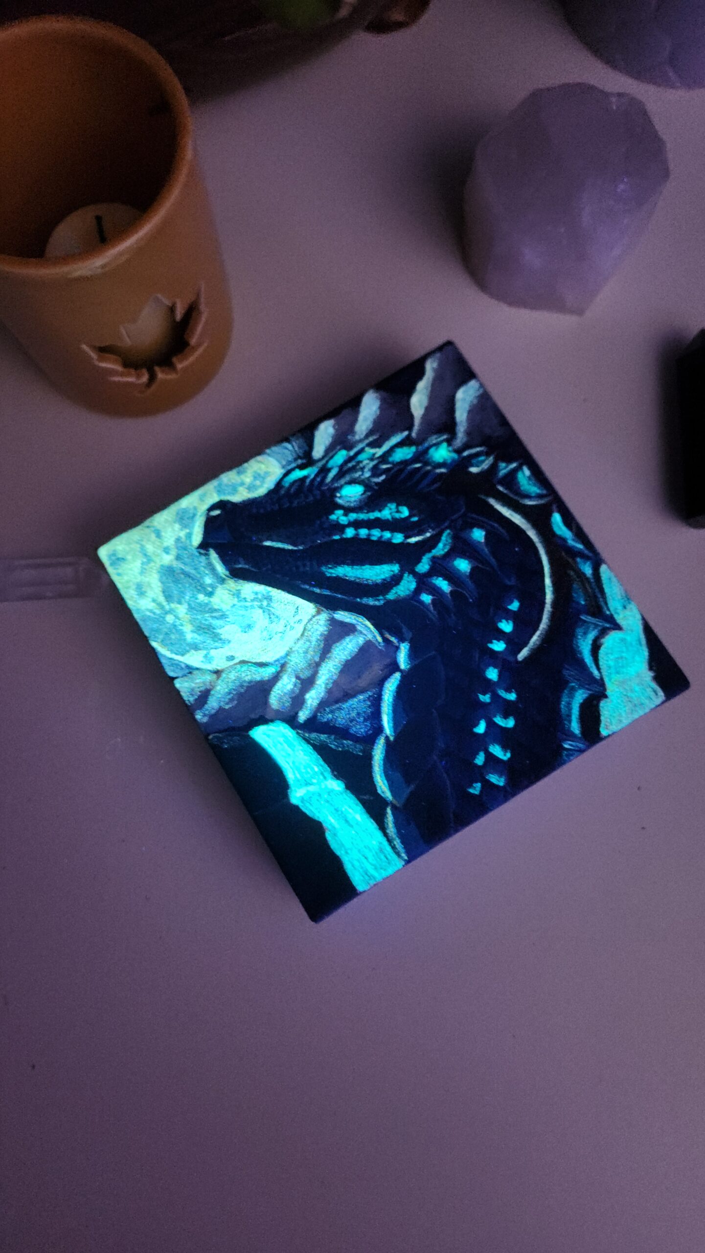 A painting of a Dragon that is flowing in the dark surrounded by candles and crystals