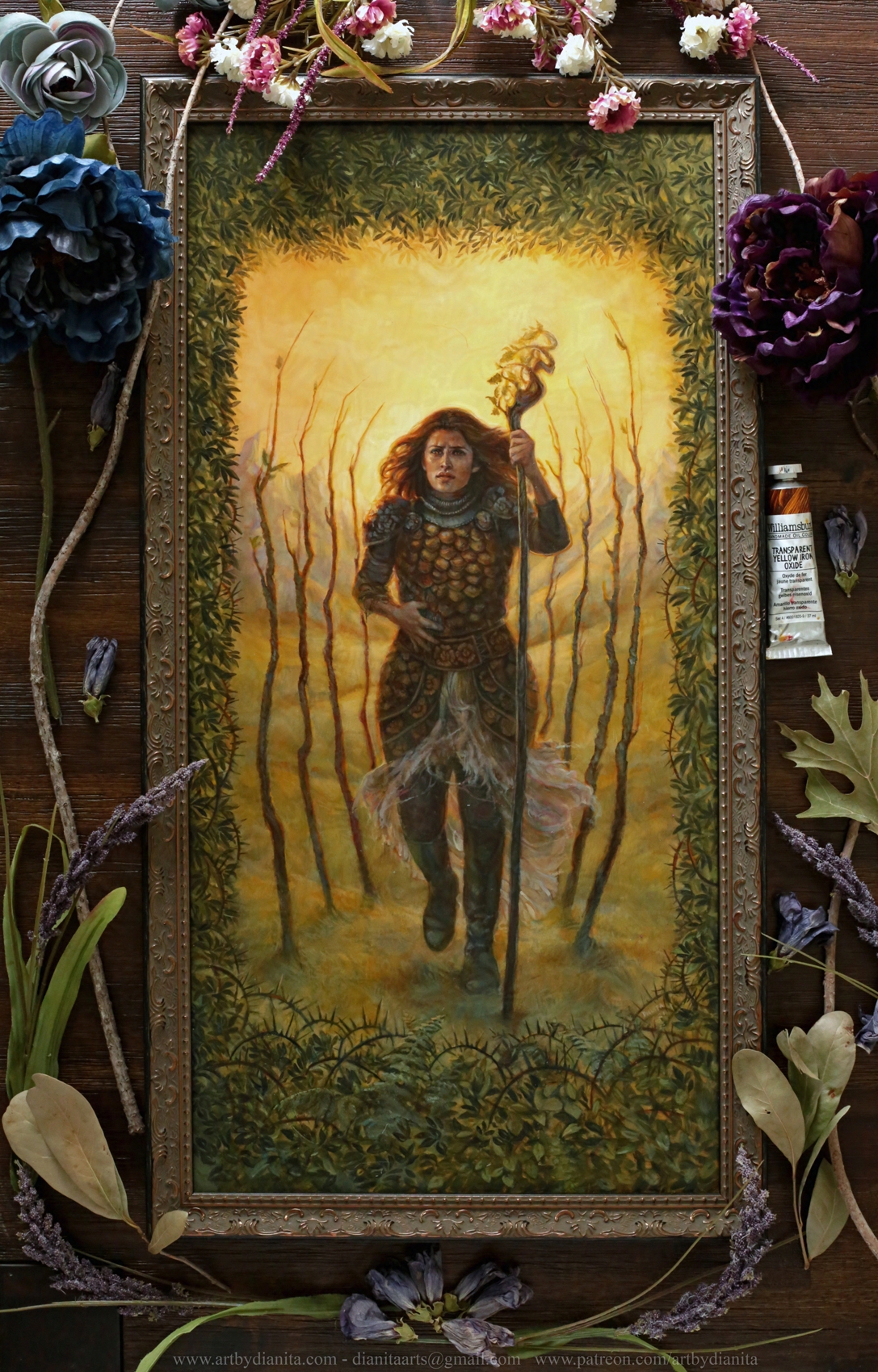 Illustration of 9 of Wands. A sorceress walks towards us, staff on left hand, hand on torso covering a wound. 4 thin trees on each side. Mountains far on the background, yellow sky. A border with leaves and on the bottom of it, thorns start to appear. This photo shows the painting framed.