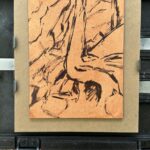 A plein-air underdrawing on a warm-toned panel showing loose brush and line work sketching the trunk and roots of a cedar tree, resting on an outdoor easel with a palette of oil paints below.