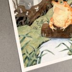 Side view with focus on signature of original artwork, photographed on neutral background with warm light