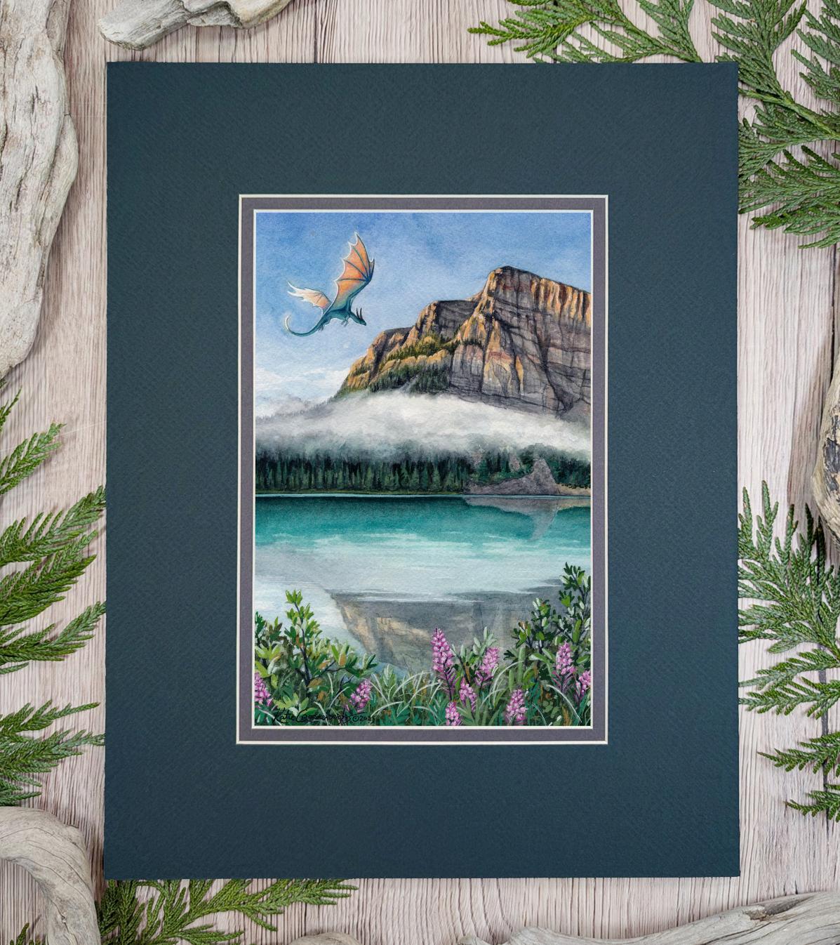 Photo of an artwork of a dragon flying over a glacial mountain lake with a cloud, plants in the foreground including fireweed flowers.