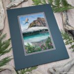 Photo of an artwork of a dragon flying over a glacial mountain lake with a cloud, plants in the foreground including fireweed flowers.