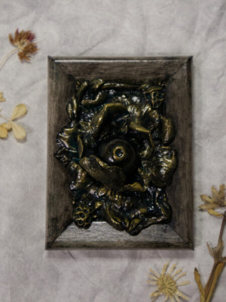 A photo of a sculpture of an eye surrounded by petals, branches, and leaves.