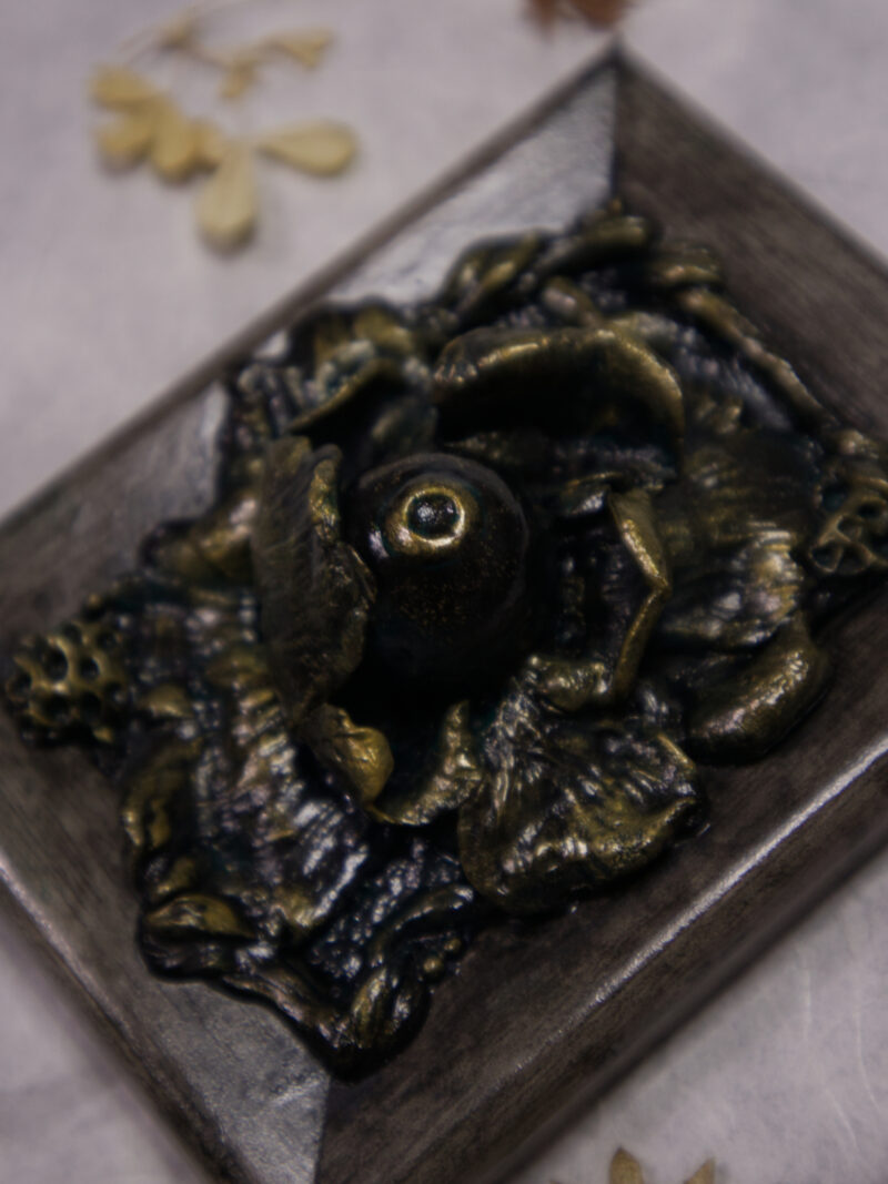 A photo of a sculpture of an eye surrounded by petals, branches, and leaves.