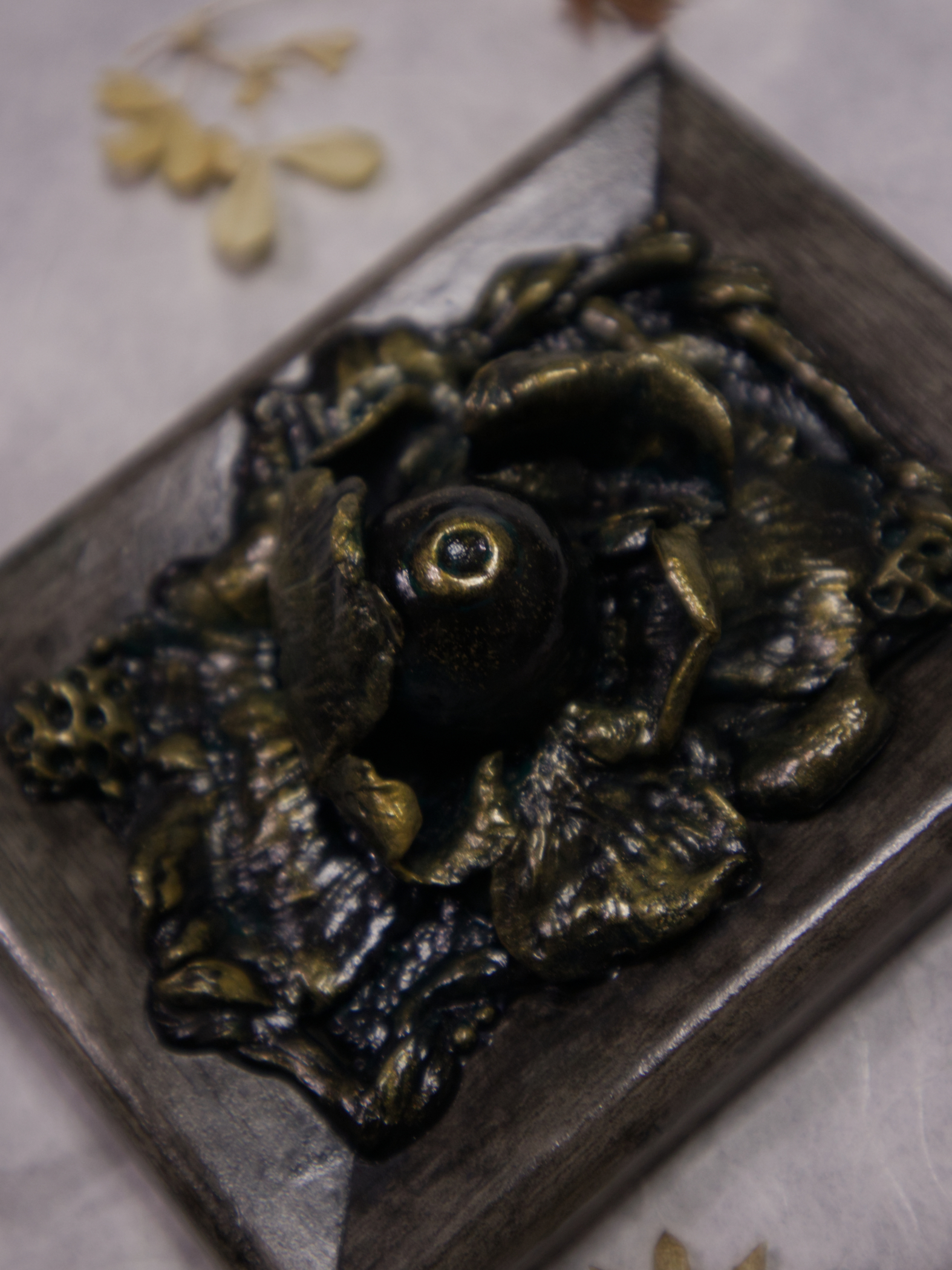 A photo of a sculpture of an eye surrounded by petals, branches, and leaves.