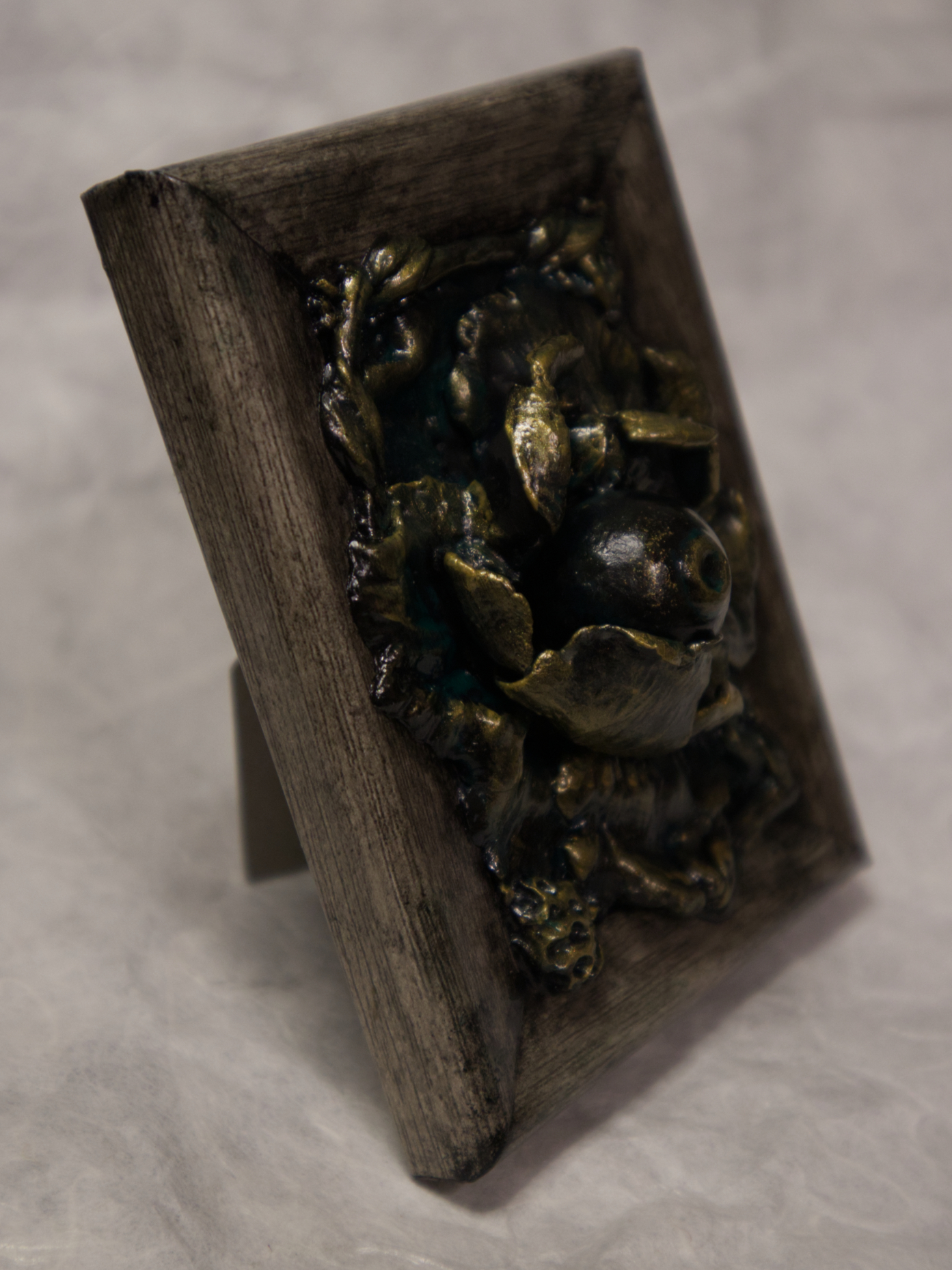 A photo of a sculpture of an eye surrounded by petals, branches, and leaves.