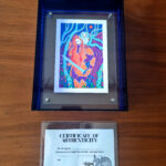 Artwork in frame with certificate of authenticity on wood table.