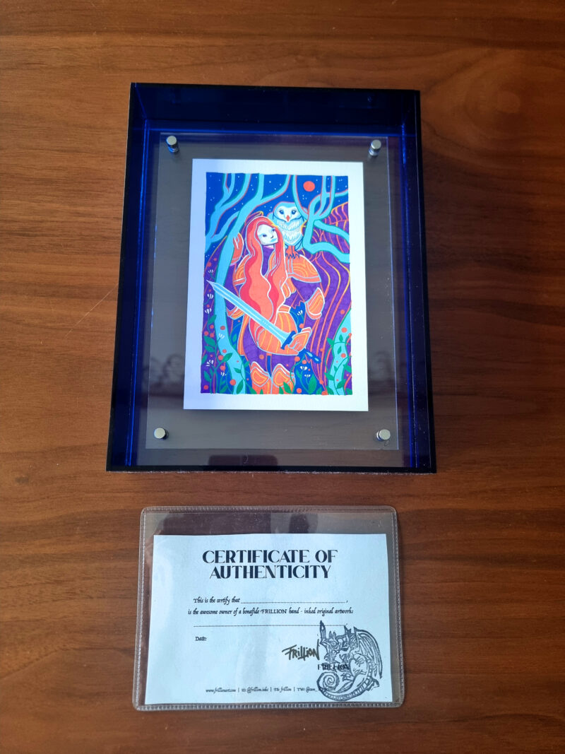 Artwork in frame with certificate of authenticity on wood table.