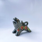 A ceramic lion sculpture with it's mouth open done with black underglaze. The piece features sgraffito Prairie Fire, a plant that looks like a fire-y paintbrush, carved onto the lion's side done with red and green underglazes.