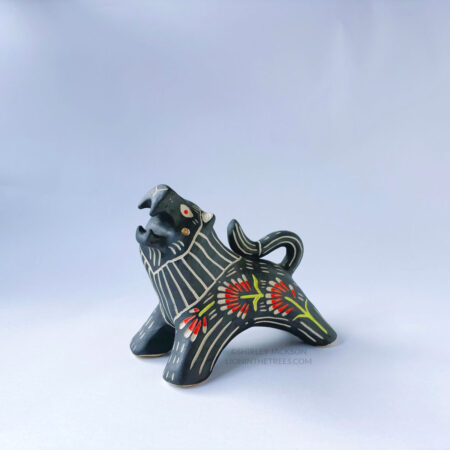 A ceramic lion sculpture with it's mouth open done with black underglaze. The piece features sgraffito Prairie Fire, a plant that looks like a fire-y paintbrush, carved onto the lion's side done with red and green underglazes.