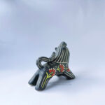 A ceramic lion sculpture with it's mouth open done with black underglaze. The piece features sgraffito Prairie Fire, a plant that looks like a fire-y paintbrush, carved onto the lion's side done with red and green underglazes.