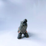 A ceramic lion sculpture with it's mouth open done with black underglaze. The piece features sgraffito Prairie Fire, a plant that looks like a fire-y paintbrush, carved onto the lion's side done with red and green underglazes.