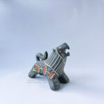 A ceramic lion sculpture with it's mouth open done with black underglaze. The piece features sgraffito Prairie Fire, a plant that looks like a fire-y paintbrush, carved onto the lion's side done with red and green underglazes.