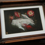 A photo of a framed painting. The frame is brown with a white mat surrounding the painting. The painting is of a white rabbit bleeding out with three white roses painted red and gold above the rabbit.