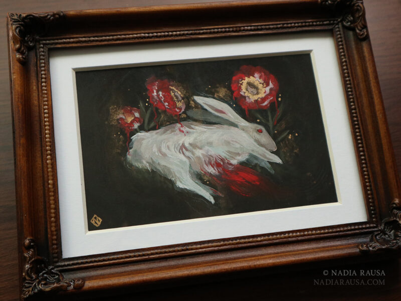 A photo of a framed painting. The frame is brown with a white mat surrounding the painting. The painting is of a white rabbit bleeding out with three white roses painted red and gold above the rabbit.
