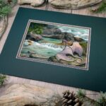 An angled view of the painting in the mat. Flat view of the illustration. A white dragon with pink and purple undertones sits on a mossy rock looking at a fish in a blue-green pool of water below a small waterfall surrounded by rocks in a river