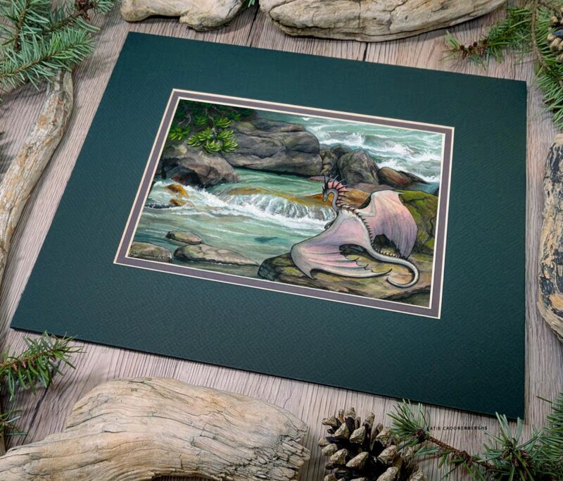 An angled view of the painting in the mat. Flat view of the illustration. A white dragon with pink and purple undertones sits on a mossy rock looking at a fish in a blue-green pool of water below a small waterfall surrounded by rocks in a river