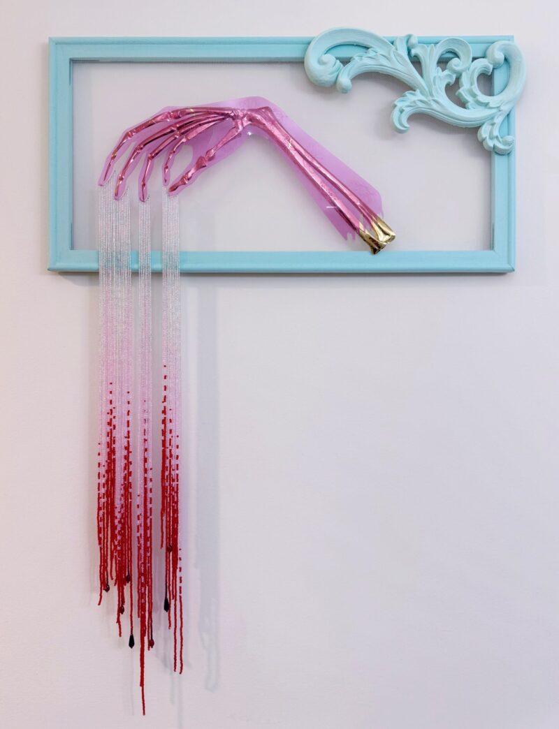 Golden skeletal hand elegantly posed with silver beads dripping from the fingers