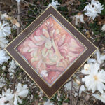 Watercolor painting of a bunny in soft pinks and greens, framed in brown wood, with magnolia flowers around it.