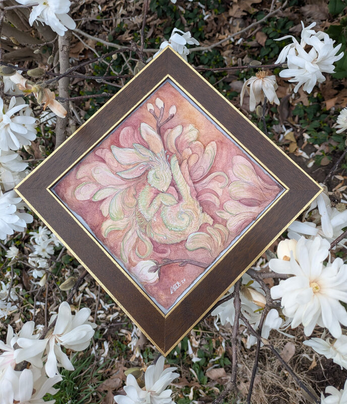 Watercolor painting of a bunny in soft pinks and greens, framed in brown wood, with magnolia flowers around it.