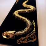 Golden snake skeleton undulates across black velvet