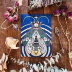 An acryla gouache painting of a lightning bug with gold leaf emanating from its glowing end. The lightning bug is on a blue background and has images of a moonflower plant drawn over its wings and body.