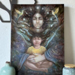 Oil painting Celestial Guardian displayed on a table in natural light, showing a celestial female figure embracing a child with two hummingbirds on either side.