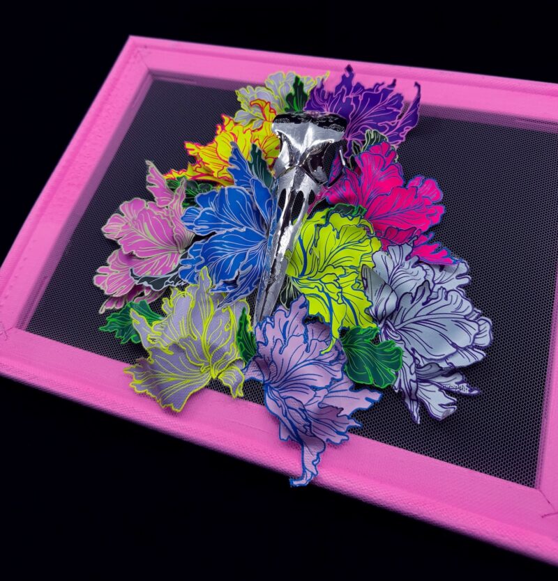 A hand-sculpted silver filigree bird skull nestled in a riot of colourful 3d flowers, hand-stitched to the frame