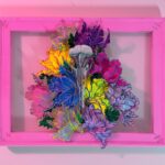 A hand-sculpted silver filigree bird skull nestled in a riot of colourful 3d flowers, hand-stitched to the frame
