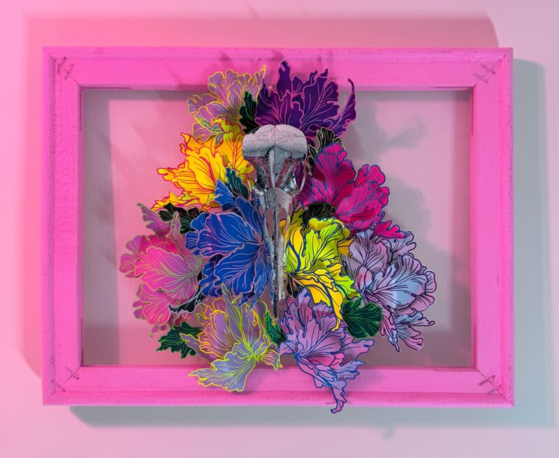 A hand-sculpted silver filigree bird skull nestled in a riot of colourful 3d flowers, hand-stitched to the frame