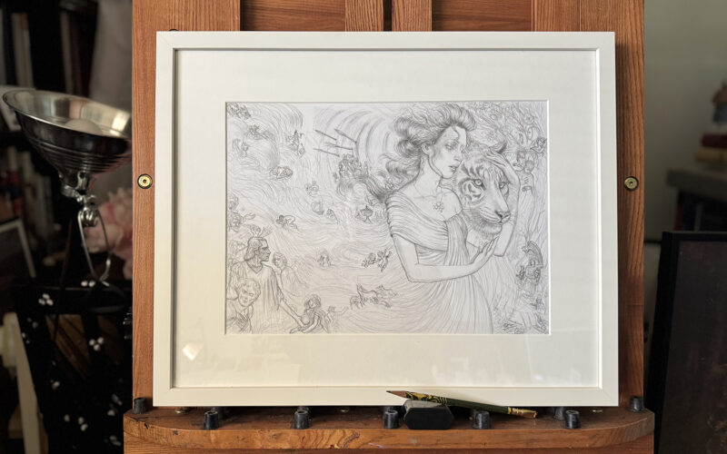Studio shot of "Strength" drawing framed and matted in white on a mahogany easel. A pencil rests in front of the framed drawing.