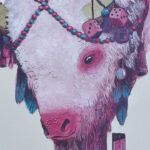 A close up of the Sacred Buffalo painting. It shows the buffalo's head and the many decorative elements such as pom poms, fuzzy dice, feathers and other ephemera.