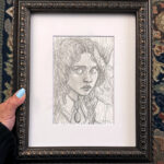 The artist's hand holds the framed 8" x 10" drawing for scale