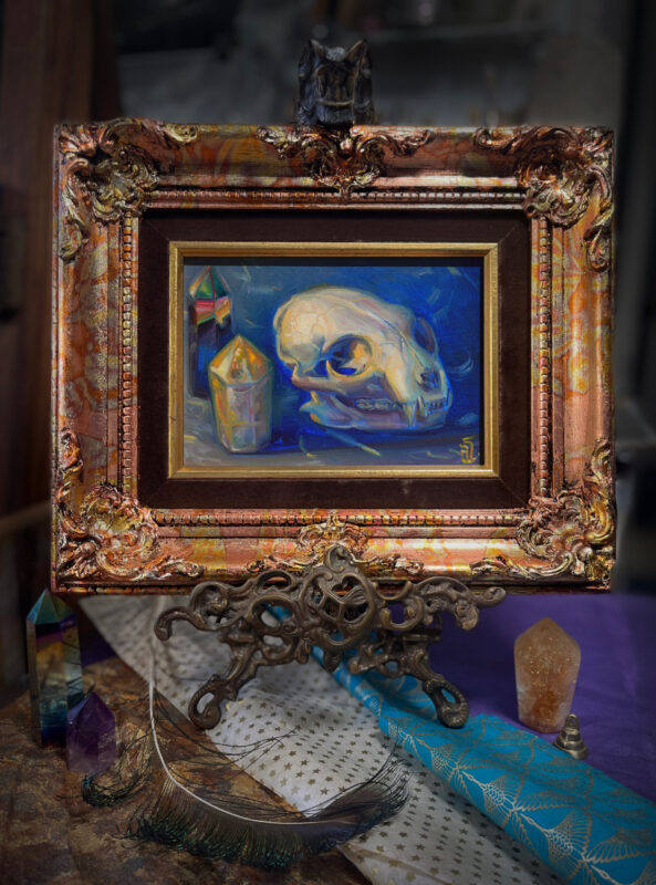 A framed oil painting of a cat skull with rainbow and citrine crystals