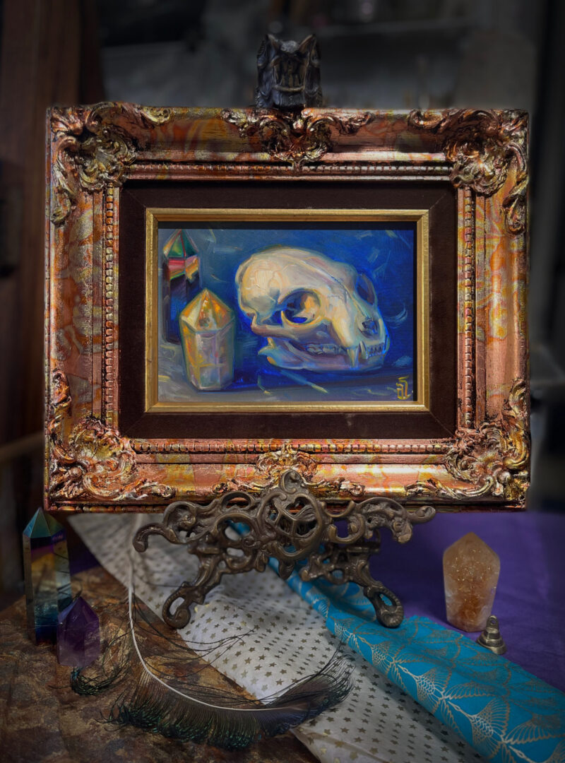 A framed oil painting of a cat skull with rainbow and citrine crystals