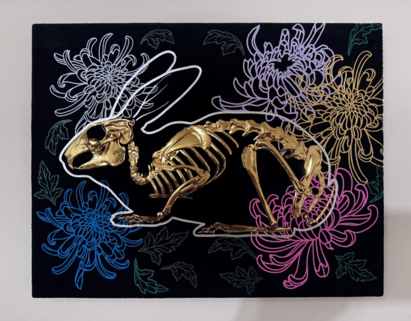 A golden bunny skeleton rests inside a burrow of chrysanthemums