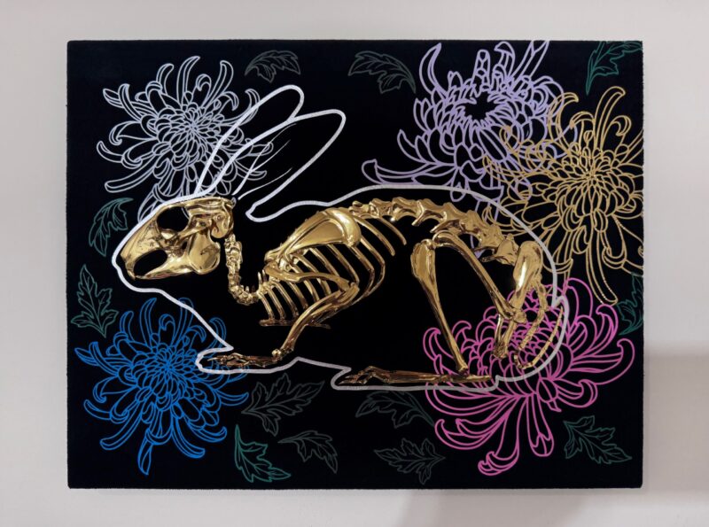 A golden bunny skeleton rests inside a burrow of chrysanthemums