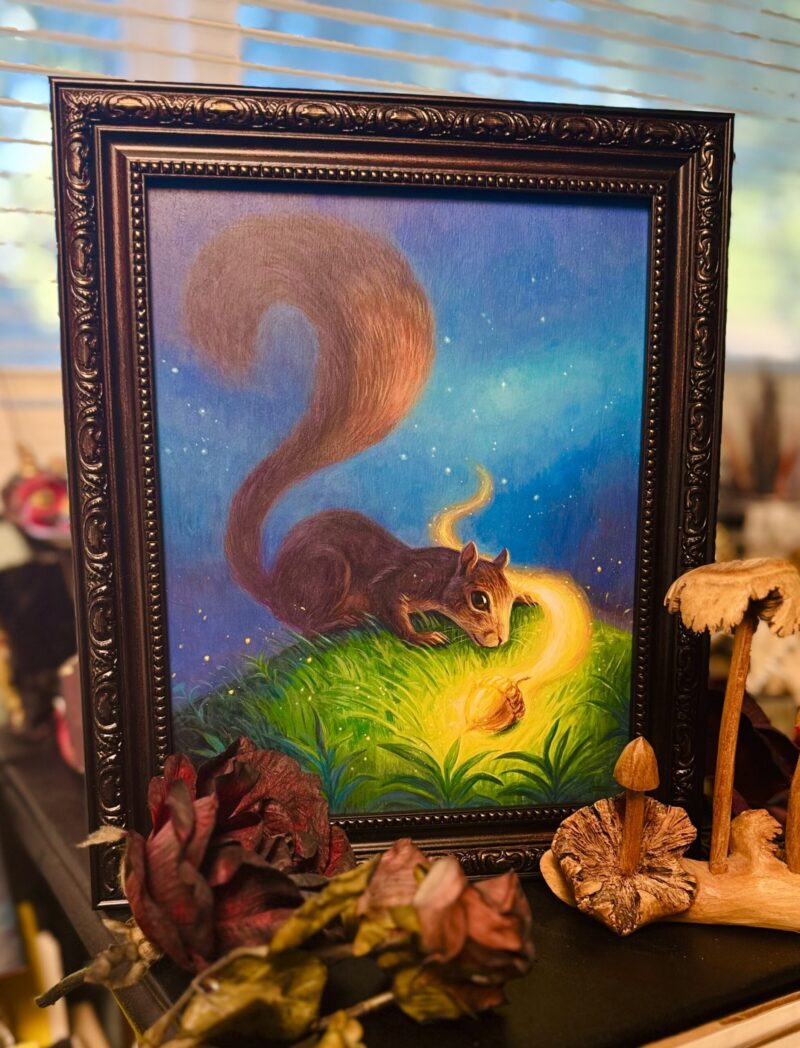 Framed squirrel painting in studio surrounded by wooden mushroom and artificial flowers on desk.