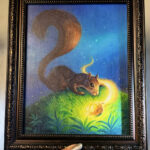 Artist's hand holding framed squirrel painting over desk for scale