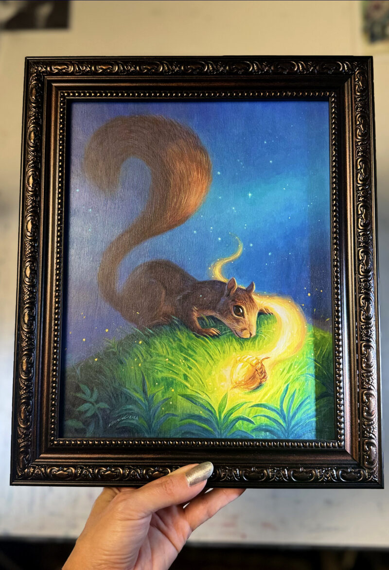 Artist's hand holding framed squirrel painting over desk for scale