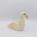 A ceramic swan sculpture done with white clay and gold luster details such as a golden beak, a constellation that runs on the side of it's chest, and floral details on the wings. This side shows a turquoise coloured eye.